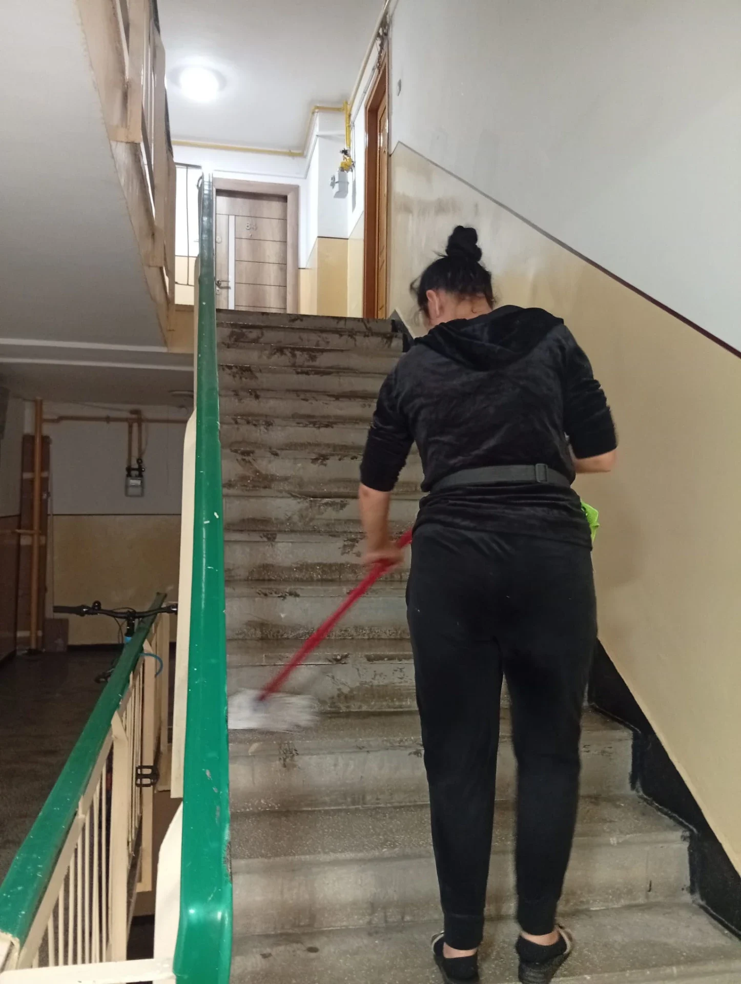 Angajată Mopul Zâmbitor spălând treptele unui bloc